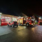 mehrere Feuerwehreinsatzfahrzeuge in der Dunkelheit vor einer hell erleuchteten Feuerwache