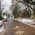 Straße mit Schneematsch bedeckt, an den Seiten Baustellenaufsteller und Bäume