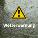 gelbes Warndreieck, Beschriftung Wetterwarnung. Im Hintergrund prasselt Regen auf grauen Boden