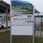 Ortseingangsschild von Gronig, weißes Schild mit Foto des Blicks über Gronig ; Herzlich Willkommen in Gronig, Schild, das die deutsch-französische Freundschaft zwischen den Partnergemeinden Oberthal und Moyenmoutier beschreibt. Weiteres weißes Schild.