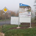 Ortseingangsschild von Güdesweiler, weißes Schild mit Foto der Güdesweiler Kirche; Herzlich Willkommen in Güdesweiler, Schild, das die deutsch-französische Freundschaft zwischen den Partnergemeinden Oberthal und Moyenmoutier beschreibt. Weiteres weißes Schild.